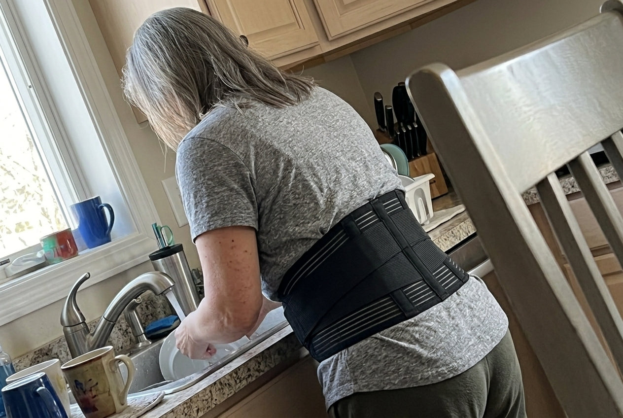 Sarah at the kitchen sink wearing a lumbar support brace, seen from behind